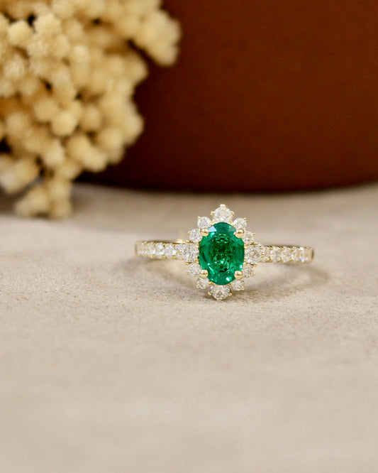 bague de fiançailles ornée d'une émeraude taille ovale, entourée de diamants. monture en or jaune 18K