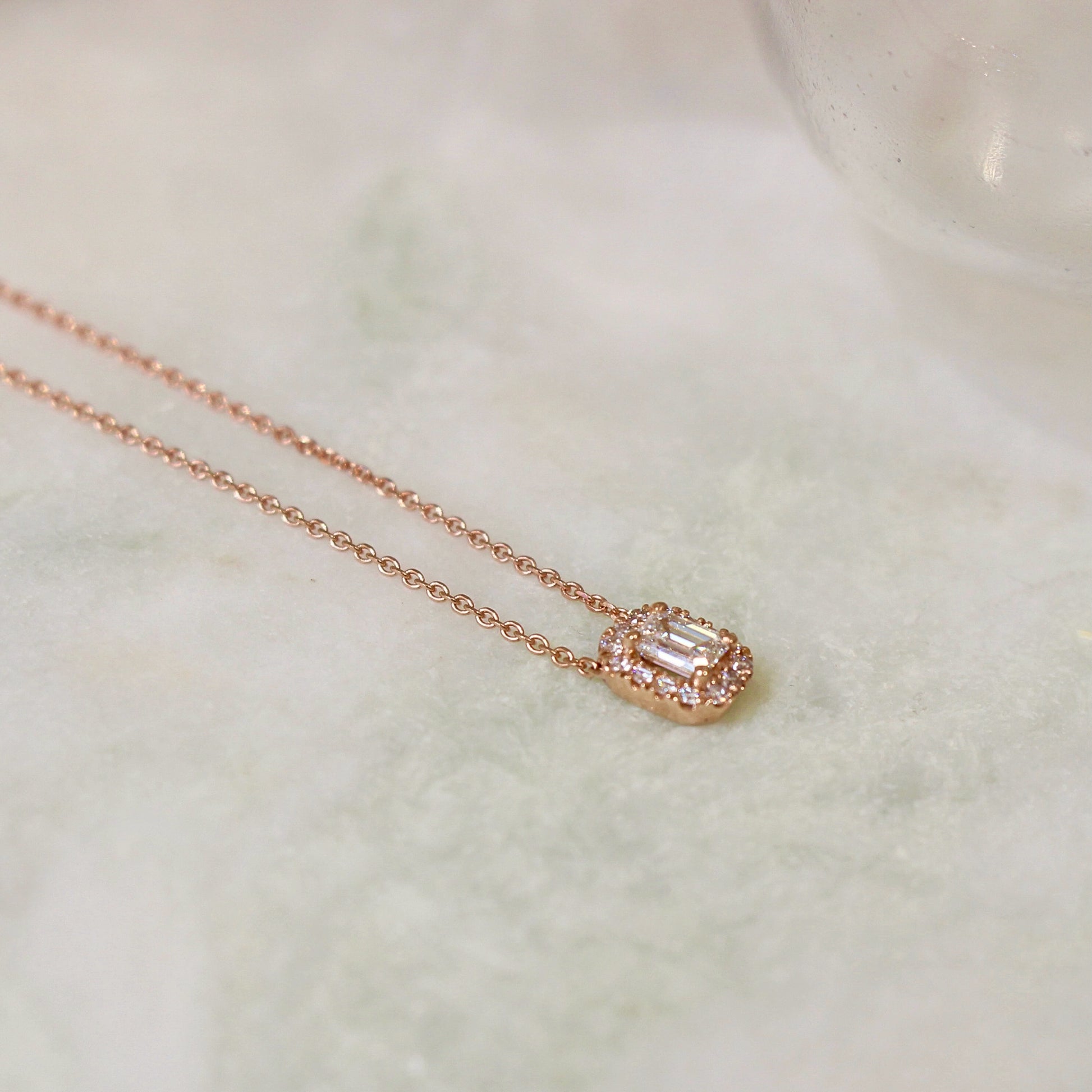 Collier pour femme en or rose avec un pendentif diamant taille émeraude et un entourage de diamants