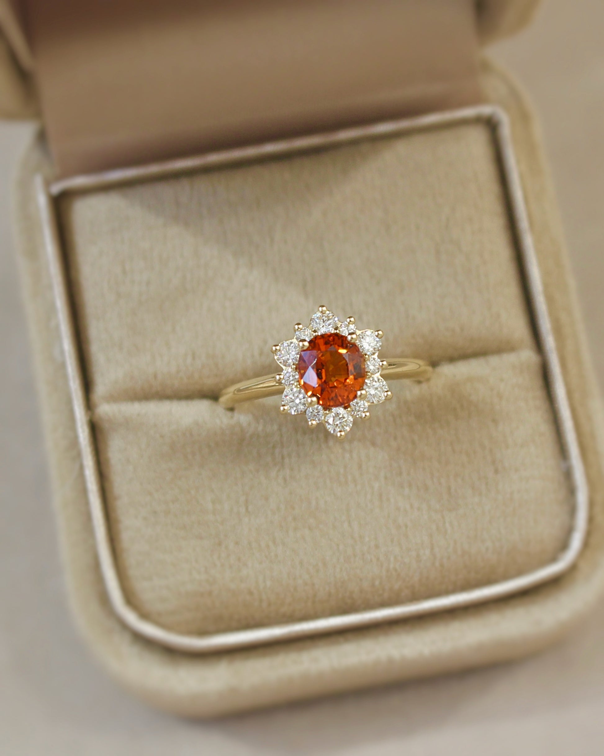 bague de fiançailles avec un grenat spessartite taille oval et un entourage de diamants sur une monture en or jaune
