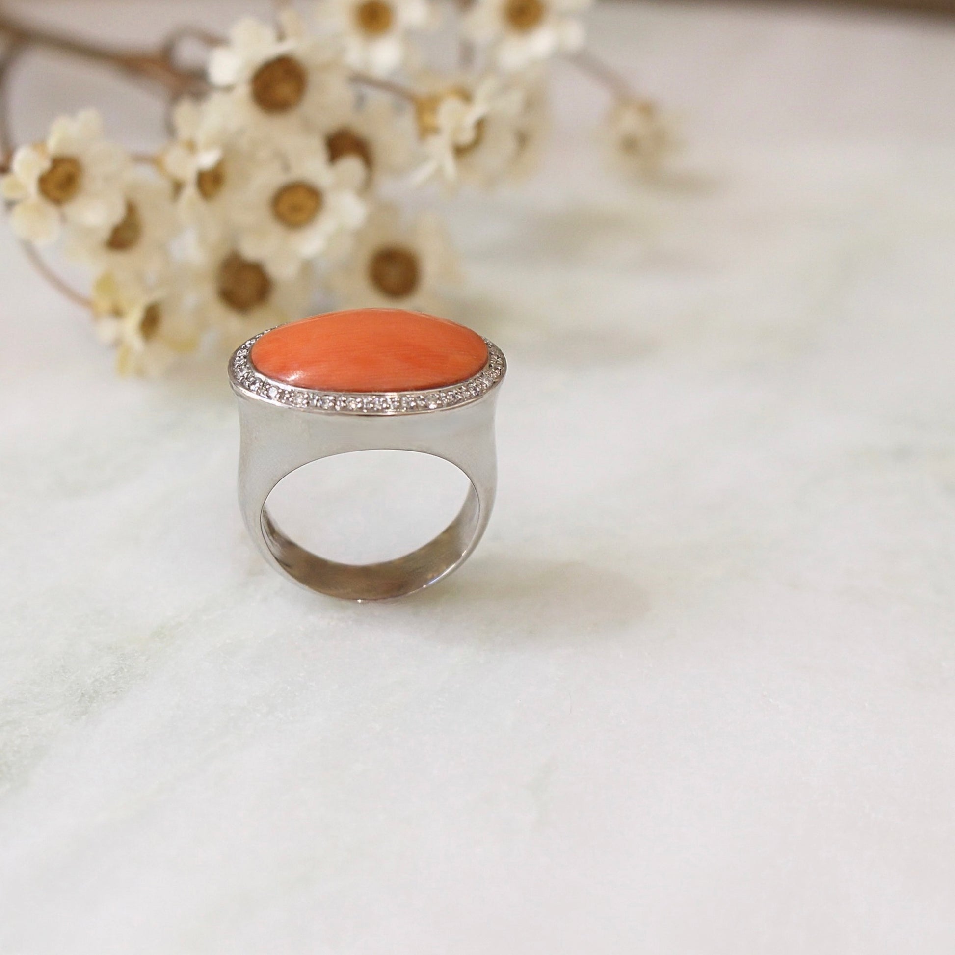 dans le style art déco une bague chevalière pour femme avec un important cabochon de corail et un entourage diamants sur une monture en or blanc 18Ke