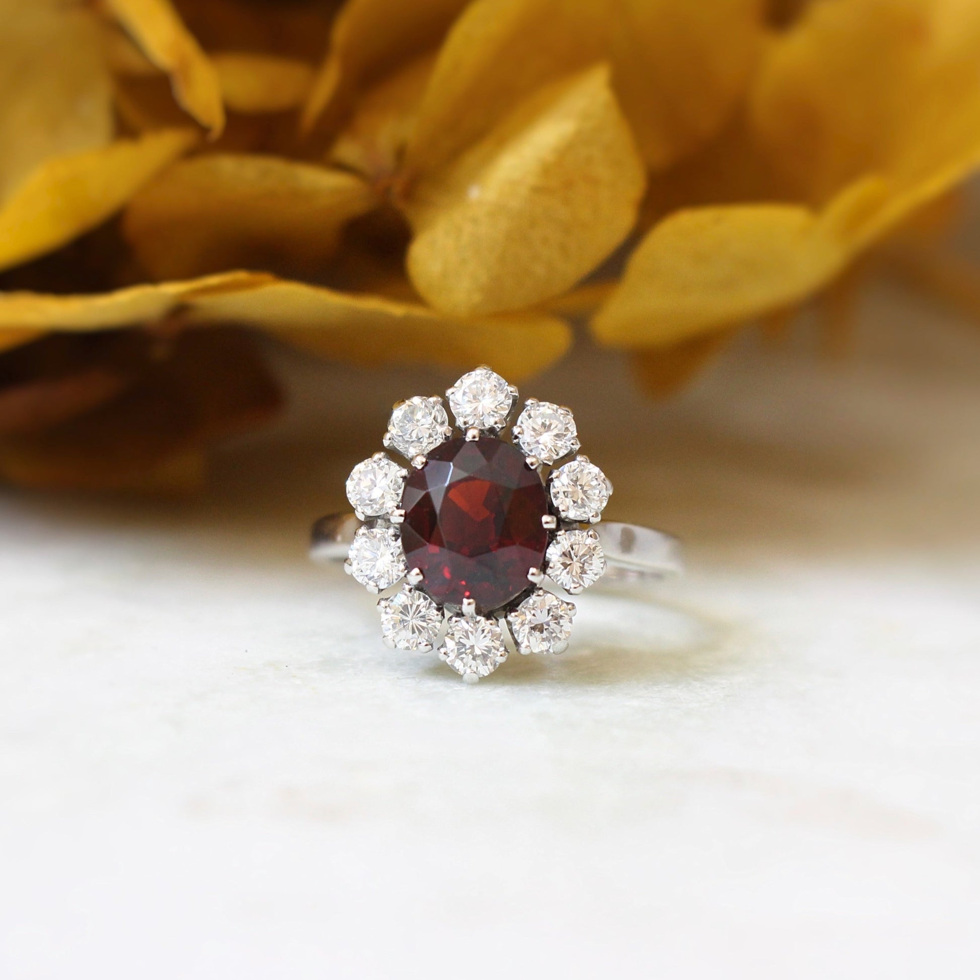 bague marguerite vintage ornée d'un magnifique grenat rhodolite taille oval entouré de 10 diamants taille brillant-monture en or blanc 18k