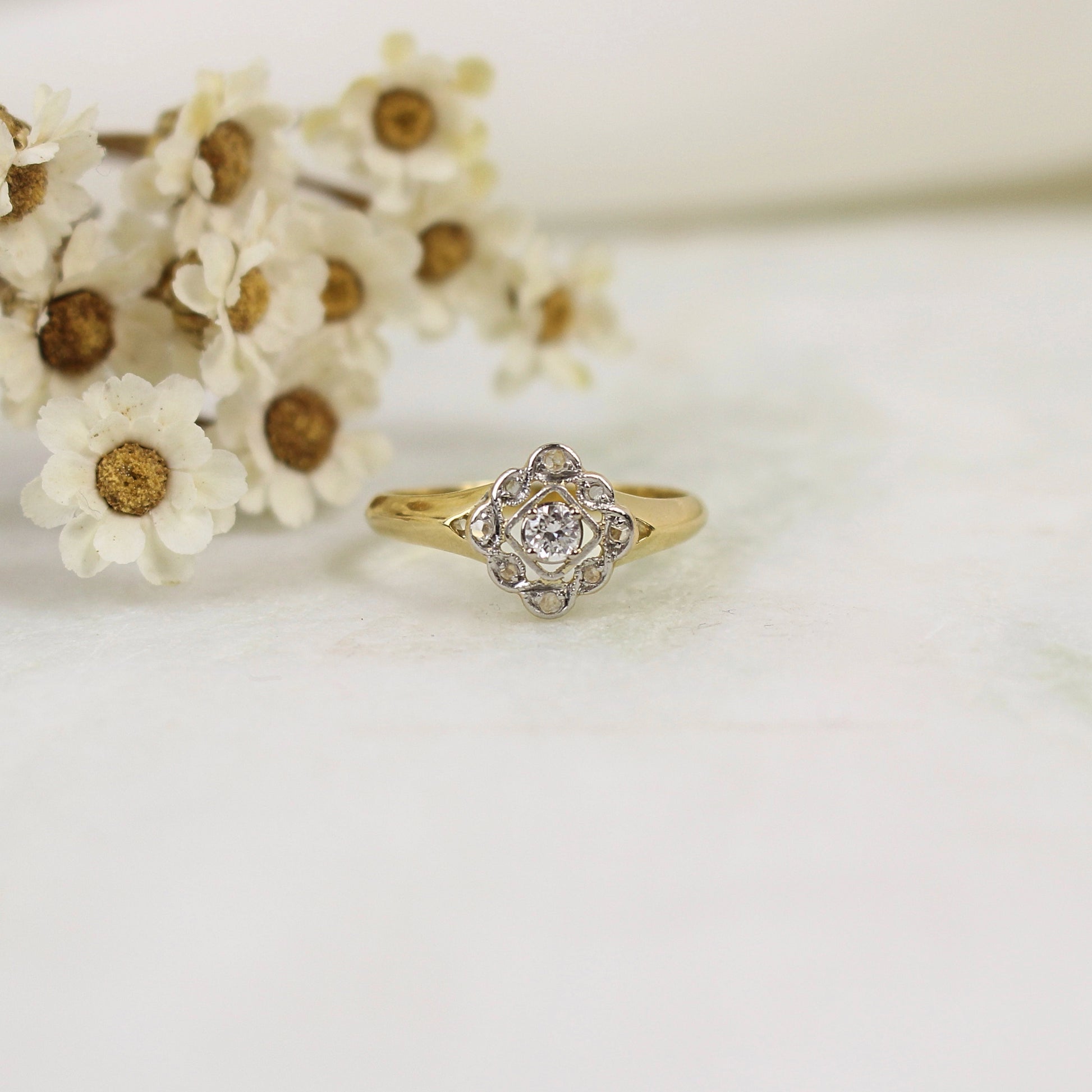 Très jolie bague losange esprit fleur avec un panier ajouré. Les pétales sont ornés de diamants taillés en rose et chaque pétale est entouré par un fil de platine filigrané.